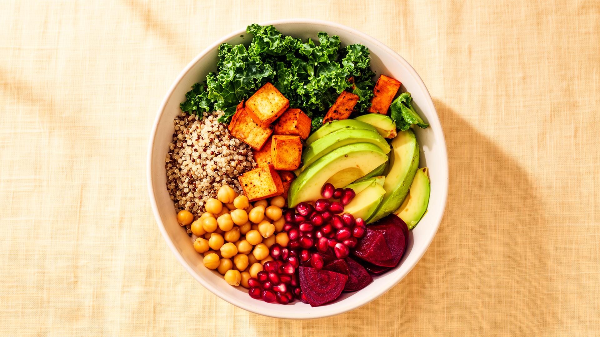 Colorful plant-based power bowl with tofu, quinoa, kale, avocado, beets and pomegranate